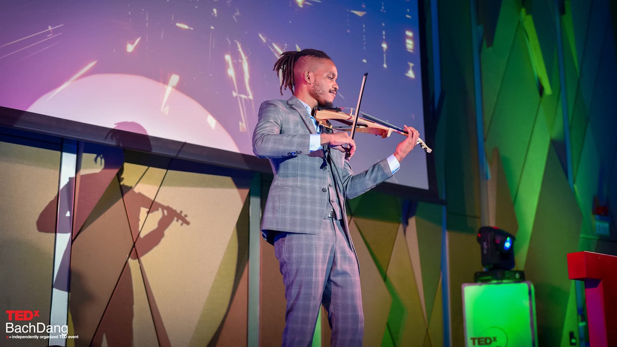 Rahmaan Phillip mid-performance on stage, violin raised, under coloured light.